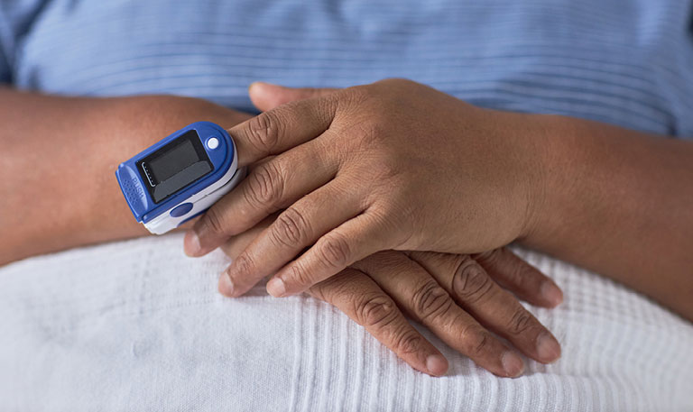 A closeup of a patient of color in a hospital with a pulse oximeter device on hand