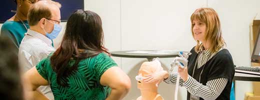 An instructor demonstrates use of ventilation equipment while two learners observe