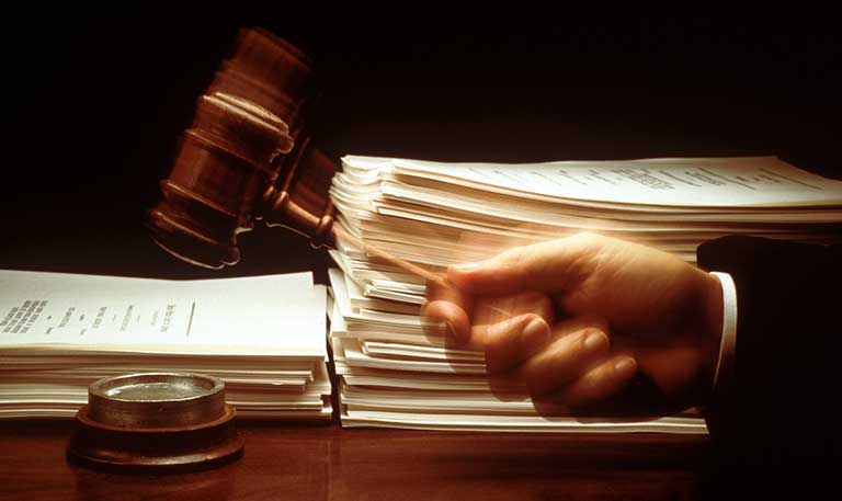 A hand banging a gavel with stacks of legal papers in the background