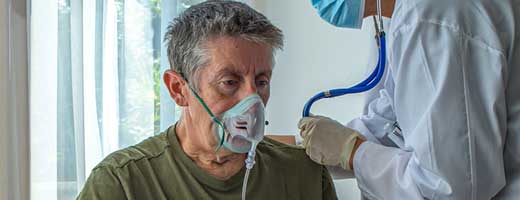 A person in a white lab coat tends to a patient with a mask on