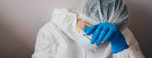 Health care provider in personal protective equipment sits on the floor, head in hands