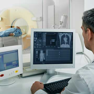 A person in a white lab coat reviews CT scans with a patient in the background
