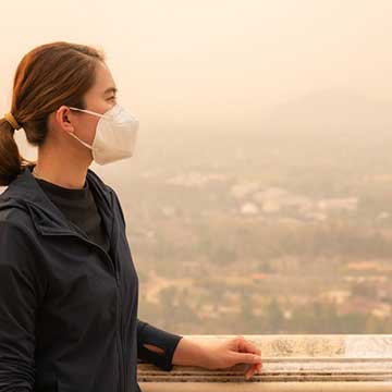 A woman stands outside with a mask on